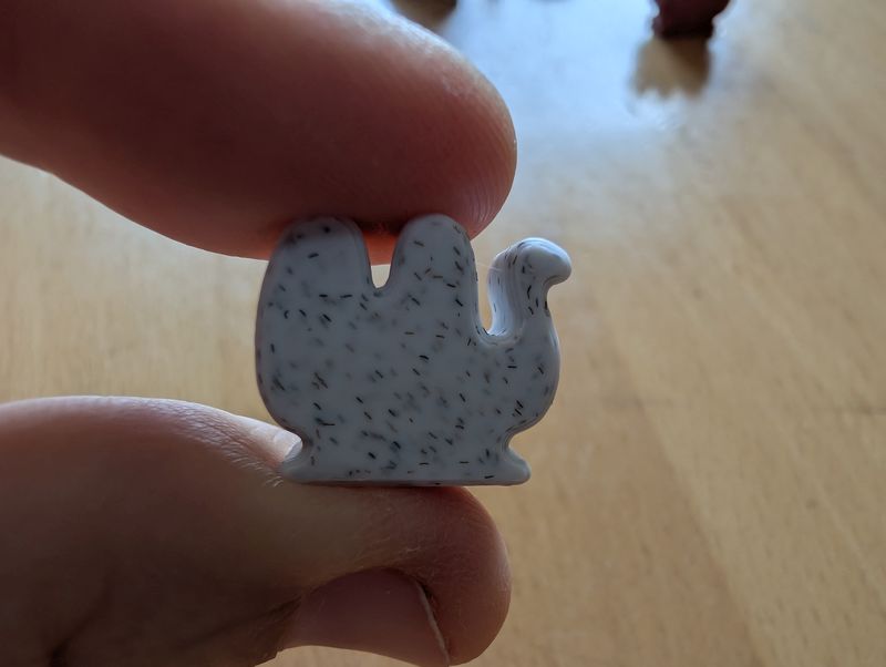 Weißer Kamelspielstein zwischen zwei Fingerspitzen